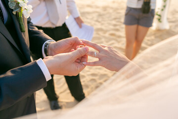 The groom is wearing a diamond ring on the bride's ring finger. at the seaside wedding There is a...