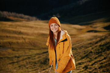 Woman running up the hill to the camera smile with teeth in the mountains in the autumn in a yellow raincoat and jeans happy sunset trip on a hike mountains in the snow, freedom lifestyle 