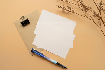 Top view of postcards, A6 off white papers and kraft envelope with a black clip and a pen. Mock up stationaries template on a orange background.