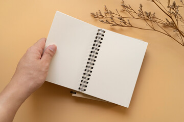 Top view of a person holding wire ring bind notebook, white paper mock up for text and notes, with dried flowers at the background
