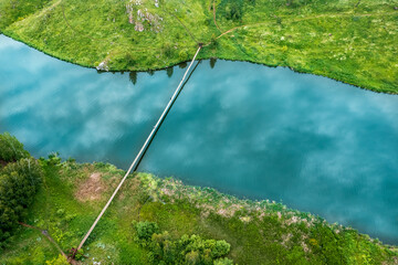 a river with banks covered with grass, a suspension bridge is thrown across the river. grass grows along the banks, the bend of the river