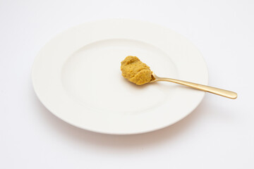 Dijon mustard spoon on white plate on white background. Hot sauce on golden spoon