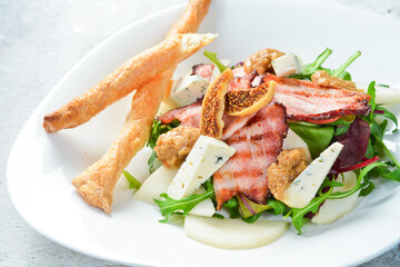 Salad with bacon, blue cheese and figs, served with grissini. On a white plate. On a gray stone background. Restaurant menu.