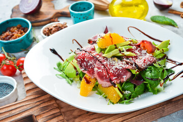 Salad: veal carpaccio, avocado, lettuce and orange. On a white plate. On a gray stone background. Restaurant menu.