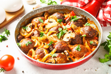 Meatballs with mushrooms in tomato sauce in a frying pan.