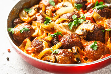 Meatballs with mushrooms in tomato sauce in a frying pan.