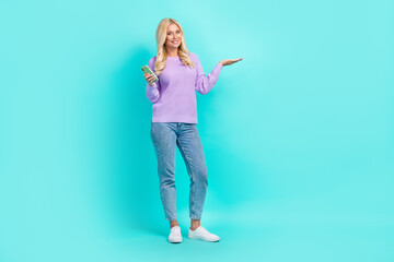 Full body photo of charming positive person hold cellphone arm show empty space isolated on aquamarine color background