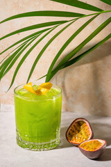 Tropical fruit cocktail in sunshine on stone background with palm leaves. Green juice shake. Gin...
