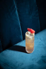 Cocktail on blue background. Modern, stylish drink placed on velvet couch at the bar, night club or...