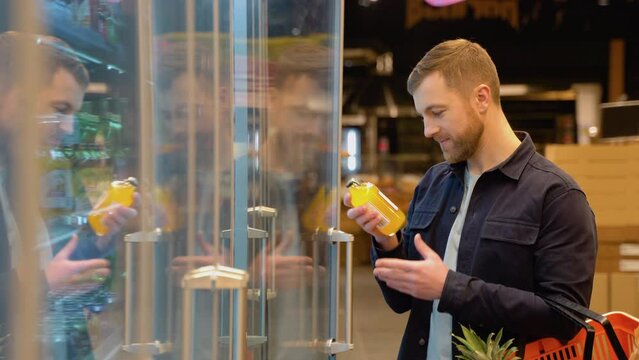 Caucasian man shopping in beverage section at supermarket. A man doing shopping at market while buying cold drink. Handsome guy holding shopping basket reading nutritional values of product
