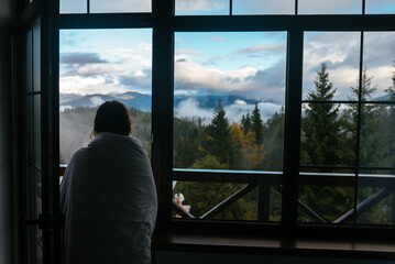 Young woman is looking through the window at the mountains