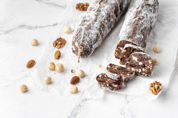 Chocolate salami filled with almonds, hazelnuts and raisins on the white background. Chocolate sweet sausage shaped dessert sprinkled with powdered sugar. Christmas and New Year festive pastry