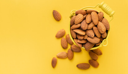 Dried almonds in a yellow bucket on the yellow background. Nuts stacked together randomly with a...