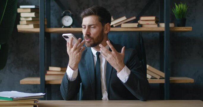Angry boss reprimands his subordinates on smartphone. Aggressive boss yelling over voice communication at his company employees in modern office. Bearded boss emotionally negotiates. Business concept