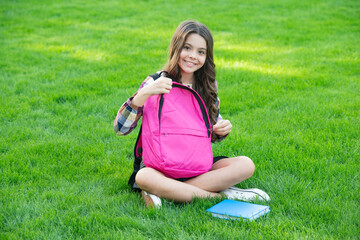 Fototapeta premium Happy teen girl opening school bag sitting on grass, education. back to school. pupil at school time