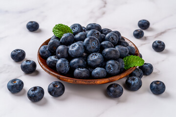 Ripe blueberry on a wooden plate over marble background. Fresh sweet blueberries for vitamin vegan snack. Wild berry as natural antioxidant for healthy eating. Vegetarian dessert.