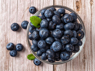 Sweet blueberries in a glass bowl over wooden surface. Ripe juicy wild berry for vitamin vegan snack. Blueberry for natural antioxidant and detox diet concept. Vegetarian dessert.