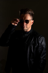 Portrait of handsome male. Sexy stylish man dressed in a leather jacket and sunglasses. Fashion hipster male isolated on grey background in studio