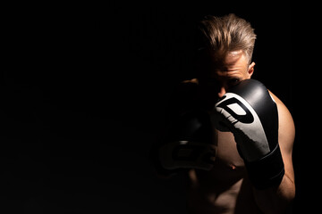 Portrait of muscular handsome topless male wearing boxing gloves isolated against a black background