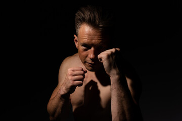 Portrait of muscular handsome topless male with his fists up ready to spar isolated against a black background