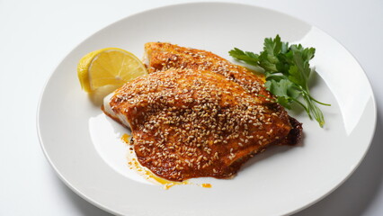 Fresh backed red tilapia fillet on white plate with lemon and herbs