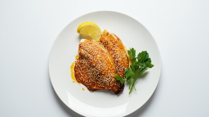 Fresh backed red tilapia fillet on white plate with lemon and herbs