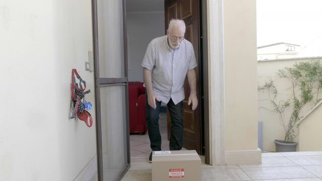 Elderly Caucasian male pensioner on the door of his house receives a postal package from the courier.