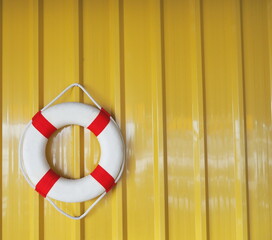 A white-red lifebuoy hanging with white manila rope on a yellow galvanized fence and space for...