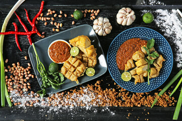 Flat lay photo of Batagor (fish cake), Indonesia's signature street food served with peanut sauce, plating in a black wooden table. 