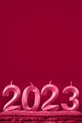 Holiday background Happy New Year. Numbers 2023 made by viva magenta candles. Minimalistic vertical red background and empty copy space for text or design. Candles without fire stuck in cake.