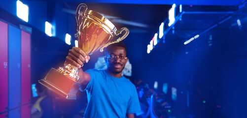 Young American African man professional gamer hold trophy cup for win in esport cybergaming, neon...