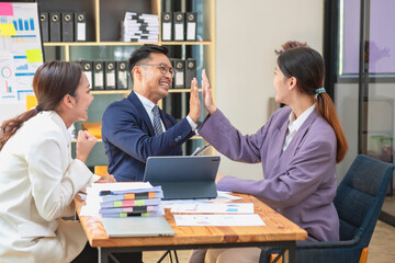 Team business three smiling and happy Asian men and women team using tablets and laptops brainstorm and plot statistics on a corporate chart board inside the company. Colleagues concept.