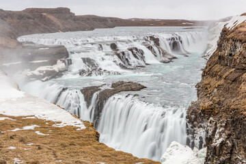 panoramica di Gullfoss, la cascata di acqua che scorre tra ghiaccio e neve in primavera durante il...