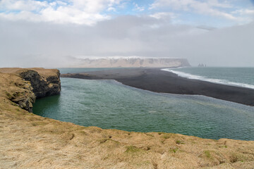 Fototapeta premium A rock outcrop that emerges from the black beach - Reynisfjara Beach