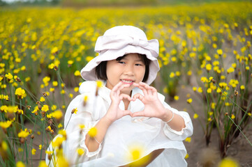 Cute Japanese,Korean Girl Kid  was wearing a white dress and a hat.Sitting in a field of bright yellow flowers, very beautiful.There is blur and bokeh in the foreground and background.