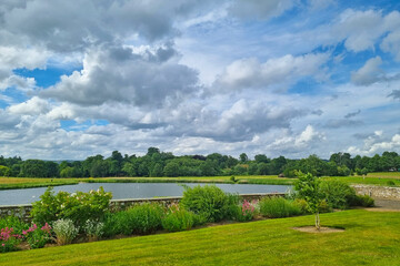 Fototapeta na wymiar Beautiful view of the lake and the green meadow in the park. A sunny summer day with large white clouds in the sky.