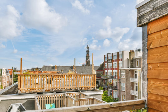 A City With Buildings And A Clock Tower In The Distance, Taken From An Apartment Balcony On A Sunny Day