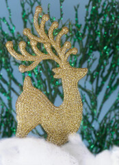 A glittering reindeer ornament on sparkly green and blue background standing in snow made of cotton balls. Christmas image.