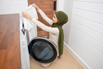 Happy young muslim woman wearing hijab doing laundry in home , healthy lifestyle concept