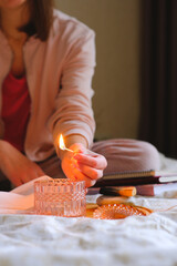 Woman lighting a candle with a match. Objects for meditation, antistress, relaxation, spiritual practice, yoga. Stick of palo santo with smudge smoke on a stone. Cozy bedroom view, diaries, books.