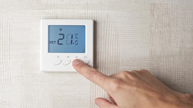 male hand turning up the temperature from 19 to 22 degrees on a digital thermostat