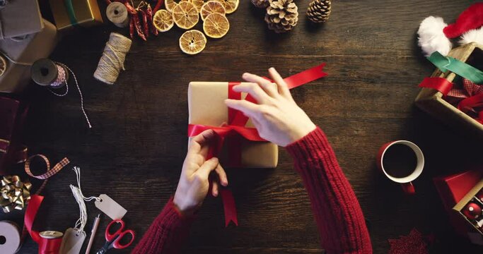 Christmas, woman and hands with gift ribbon for celebration package decoration top view. Present box and wrapping technique of festive holiday event girl busy at table with coffee drink.