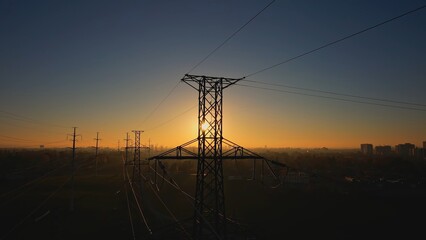 High voltage electric towers at golden hour sunset. Transmission power line and grid infrastructure. Power line insulators and wires silhouette. Energy crisis and high gas and oil prices concept.