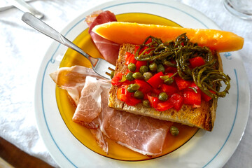 Antipasto di Natale con prosciutto, melone, bruschetta, pomodoro, capperi, salicornia e olio di oliva