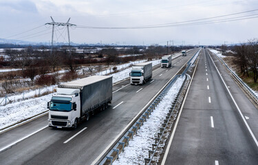 Convoy of Transportation Lorry Trucks on a Highway in a snowy winter landscape. Business Transportation And Trucking Industry.