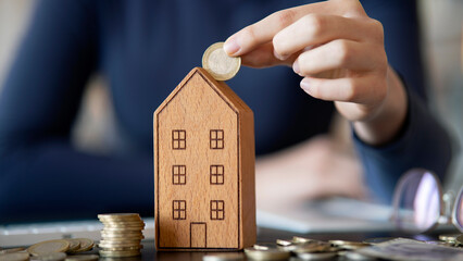 Hand putting coin in house model of coin for saving money for buying house. 