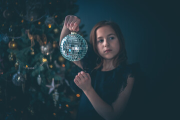 cute girl holds a disco ball against the background of a Christmas tree
