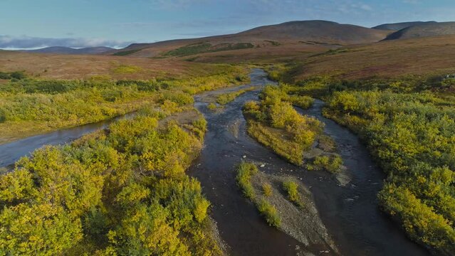 Aerial view from a drone flying forwards over tundra landscape with rolling hills and river in western Alaska