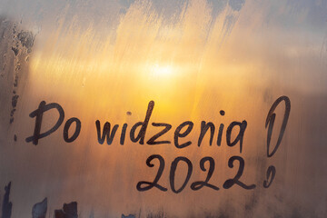 lettering Do widzenia in Polish is goodbye in english and numbers 2022 paint with finger of water on splashed by frost foggy glass on sunset window - obrazy, fototapety, plakaty