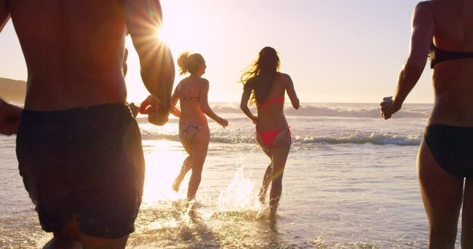Friends, beach and people running in water for fun while on holiday at sea during sunset in bikini and swimwear outdoor in nature. Men and women group together at ocean water for holiday in summer